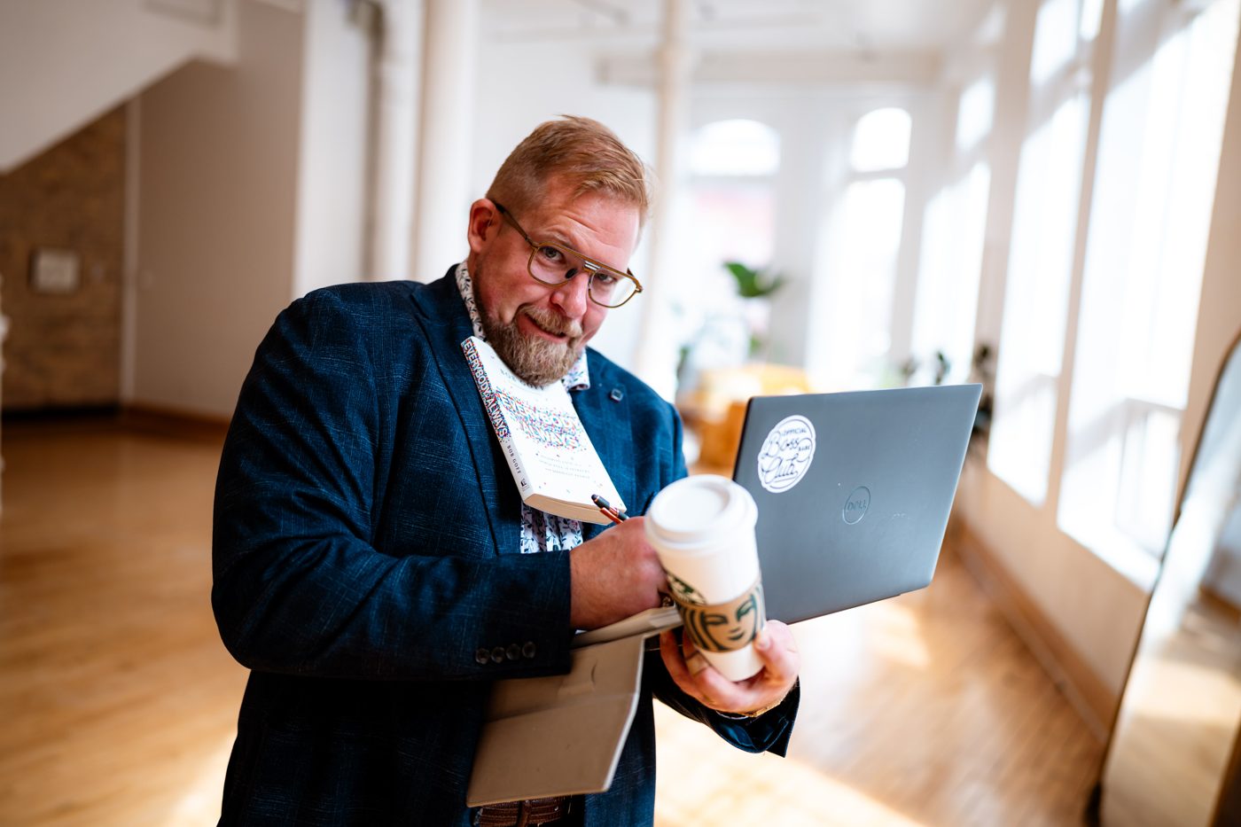 Jon grimacing while juggling a book, a coffee, a notebook and a laptop